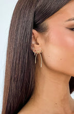 Close-up of a gold twisted metal bow earring with two hanging twisted strands ending in bars