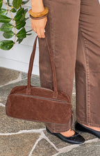 Side view of a brown suede baguette bag with leather piping and a tassel zipper pull