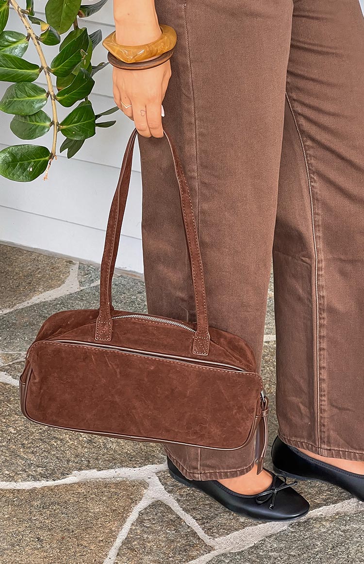 Side view of a brown suede baguette bag with leather piping and a tassel zipper pull